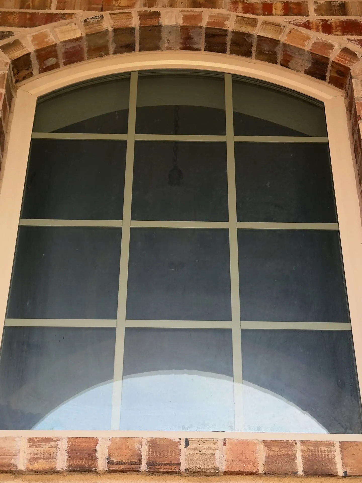 Arched window with grid pattern framed by brick and light-colored trim.